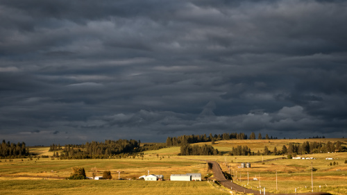 Picture of a dark sky over a bright sunlit field.